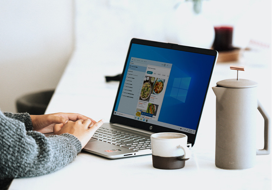 Eine Person, die auf einem Laptop IT-Leistungen recherchiert, neben einer Kaffeetasse und einer Kanne.