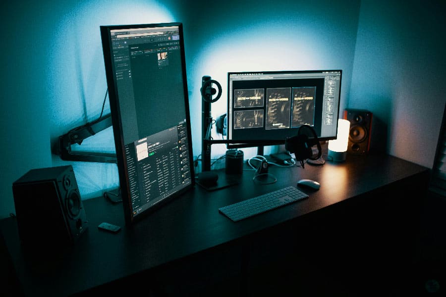 Ein moderner Arbeitsplatz mit zwei Monitoren, die Software für Performance-Monitoring anzeigen, in einem Raum mit blauer Beleuchtung.