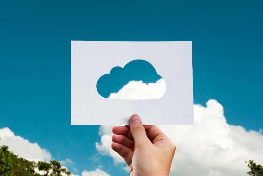 Hand hält Papier mit ausgeschnittener Wolke gegen blauen Himmel, symbolisiert Cloud Computing.