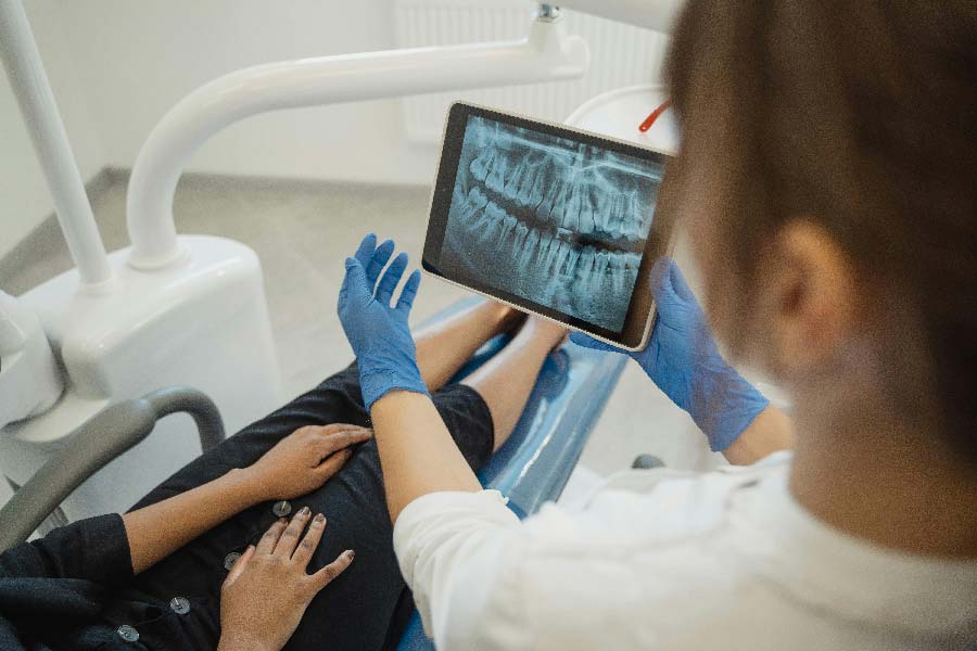 Zahnarzt zeigt Patientin Röntgenbild auf Tablet, symbolisiert Modernisierung Ihrer Zahnarztpraxis.